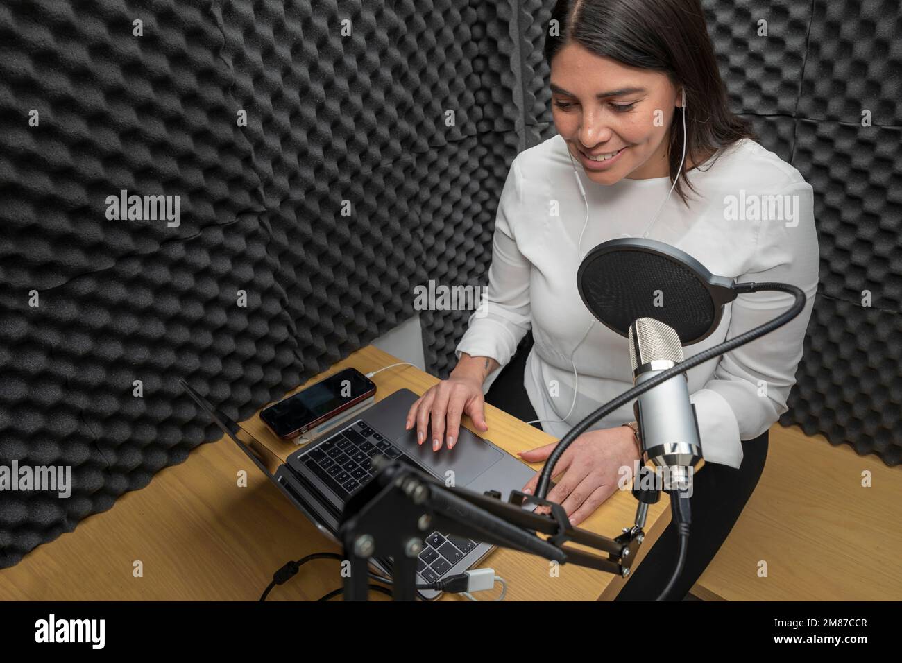 top view of a woman recording a podcast in an audio booth. Stock Photo