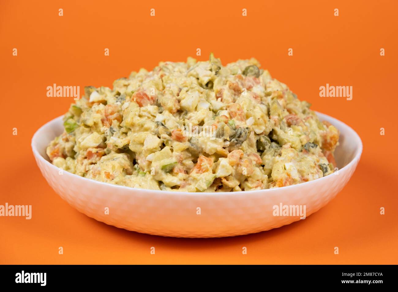 Olivier russian salad in a plate on an orange background close-up. Stock Photo