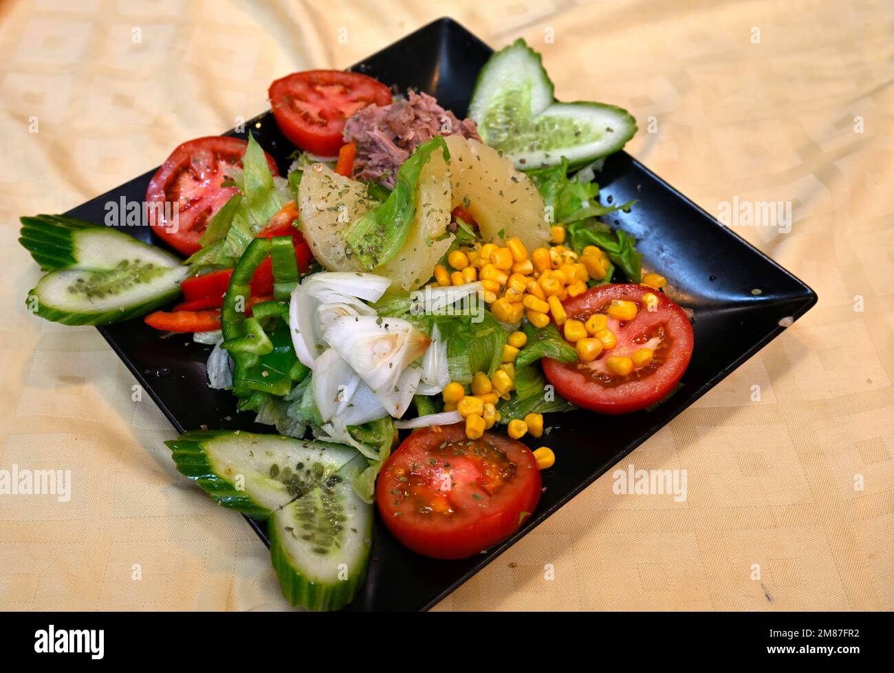 Plate of mixed salad, tomato, cucumber, onion, green pepper, corn, pineapple with oregano on black square plate Stock Photo