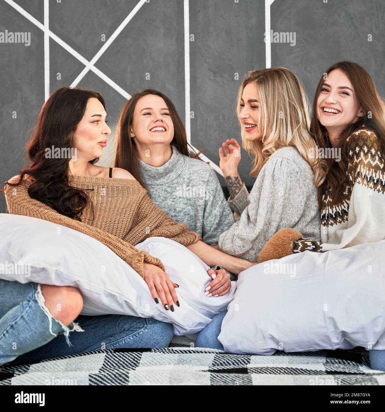 Young women enjoying winter weekends inside contemporary barn house. Four happy girls having fun on bed. Stock Photo