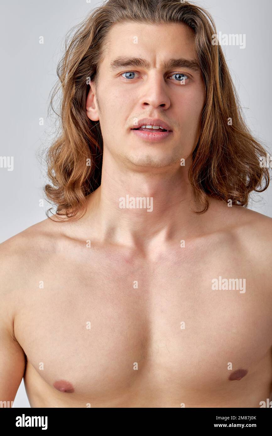 Portrait of attractive shirtless guy posing isolated over light grey color background. Long haired caucasian man with athletic torso looking at camera Stock Photo