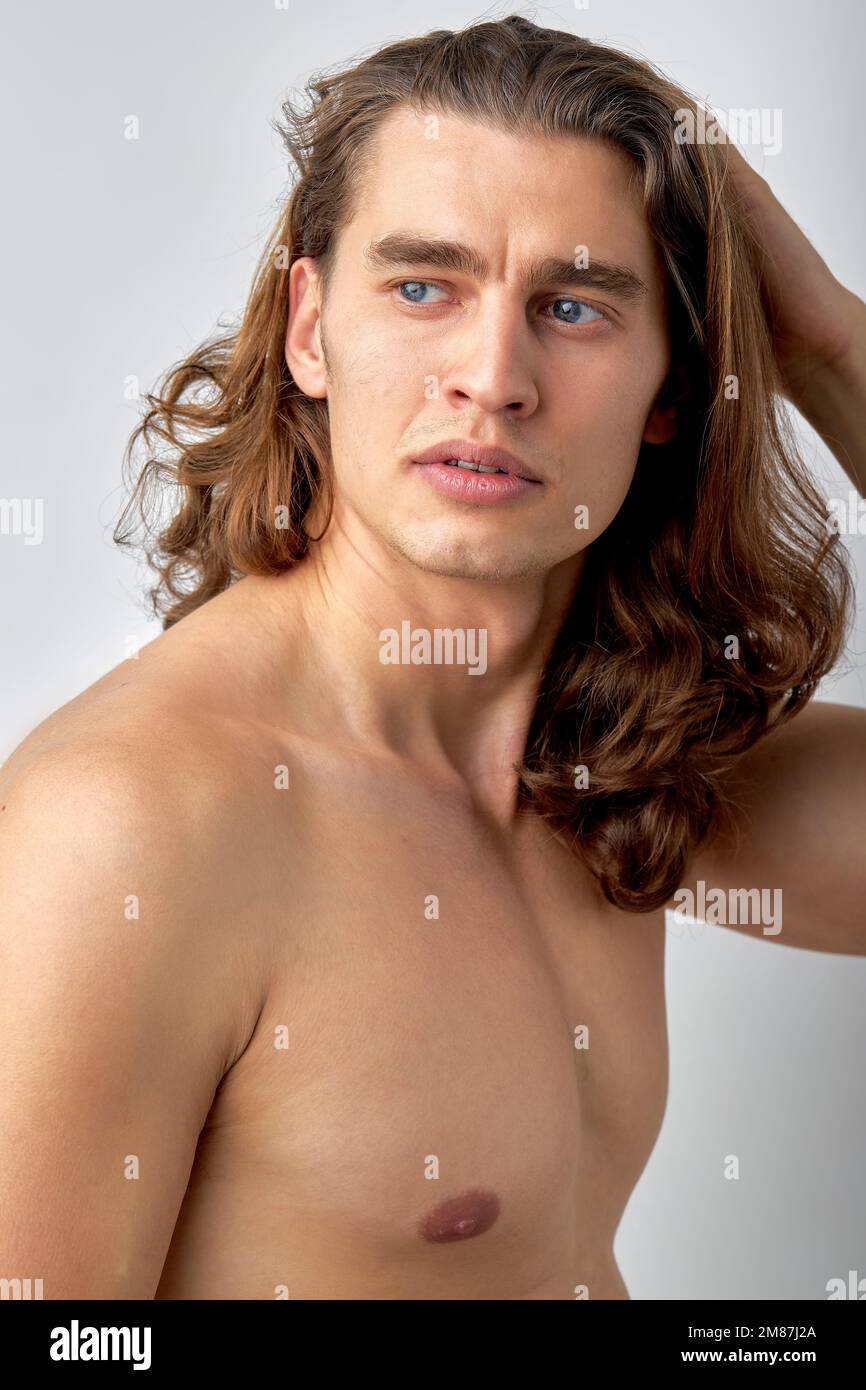 confident male model is touching long hair, head, enjoy having healthy face skin, look at side posing at camera, isolated over white studio background Stock Photo