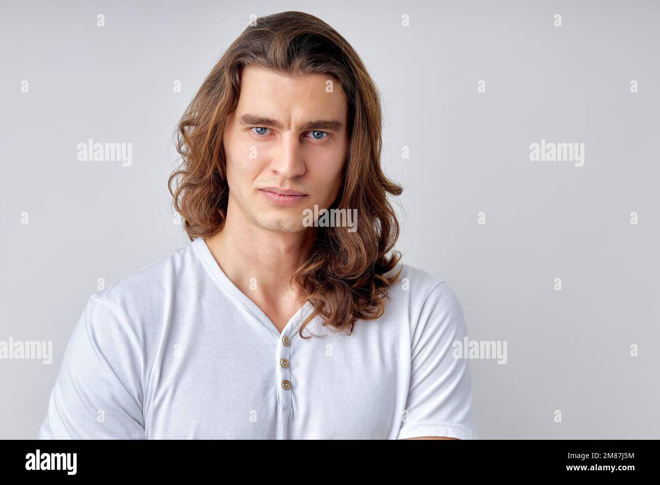 caucasian man with long hair is skeptic and nervous, disapproving expression on face. Negative person in casual white t-shirt, posing at camera. human Stock Photo