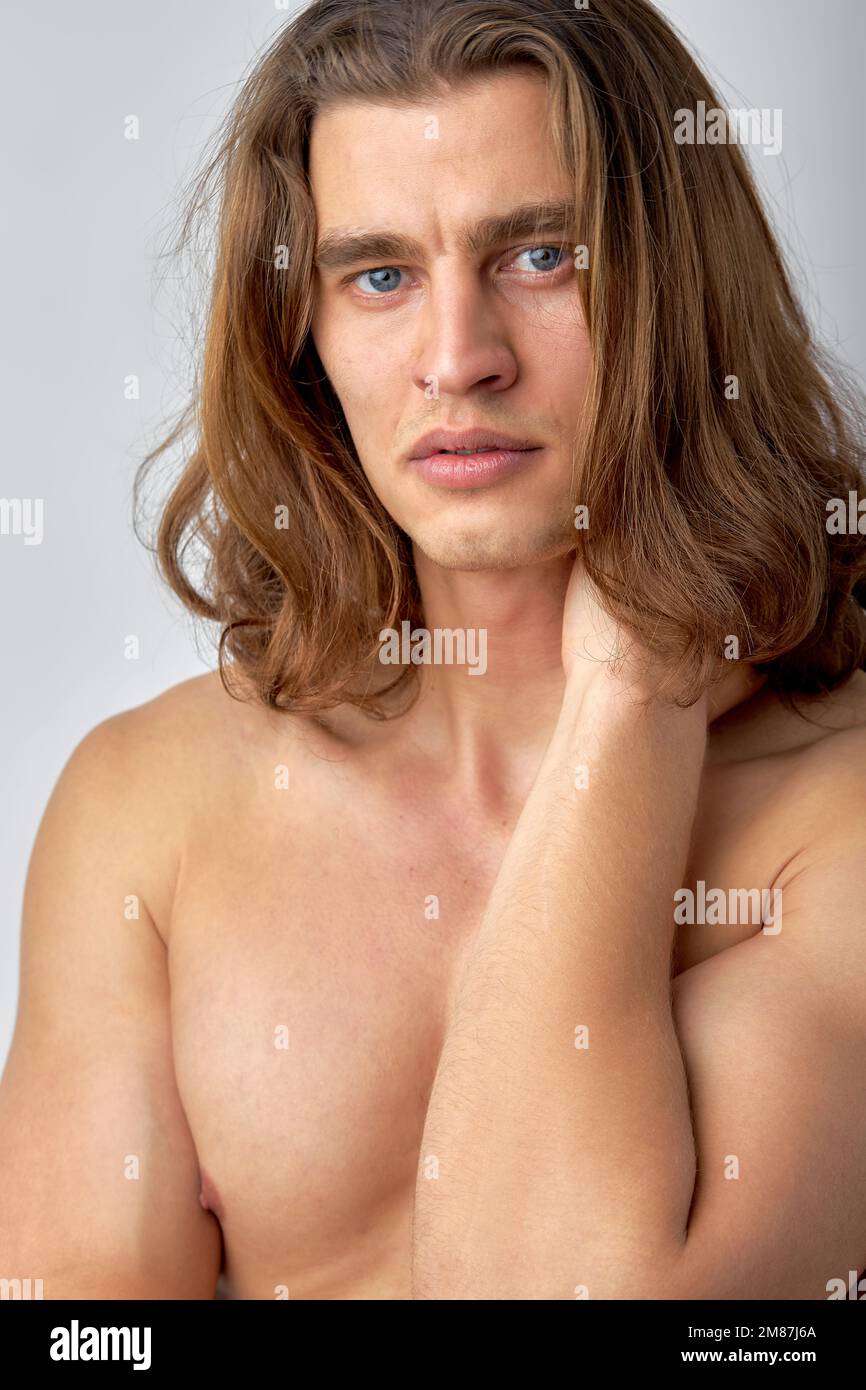 Brooding naked man looking at camera and rubbing neck isolated over white background. Young caucasian guy with long hair posing at camera, looking tho Stock Photo