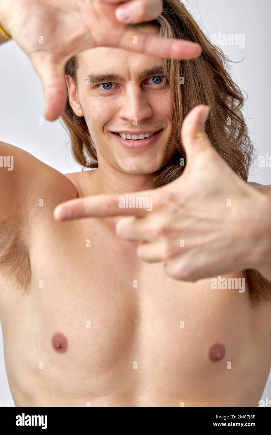 naked fit male with long hair posing at camera, half-naked man looks at camera, making shape of square like a photographer, smiling happily. isolated Stock Photo