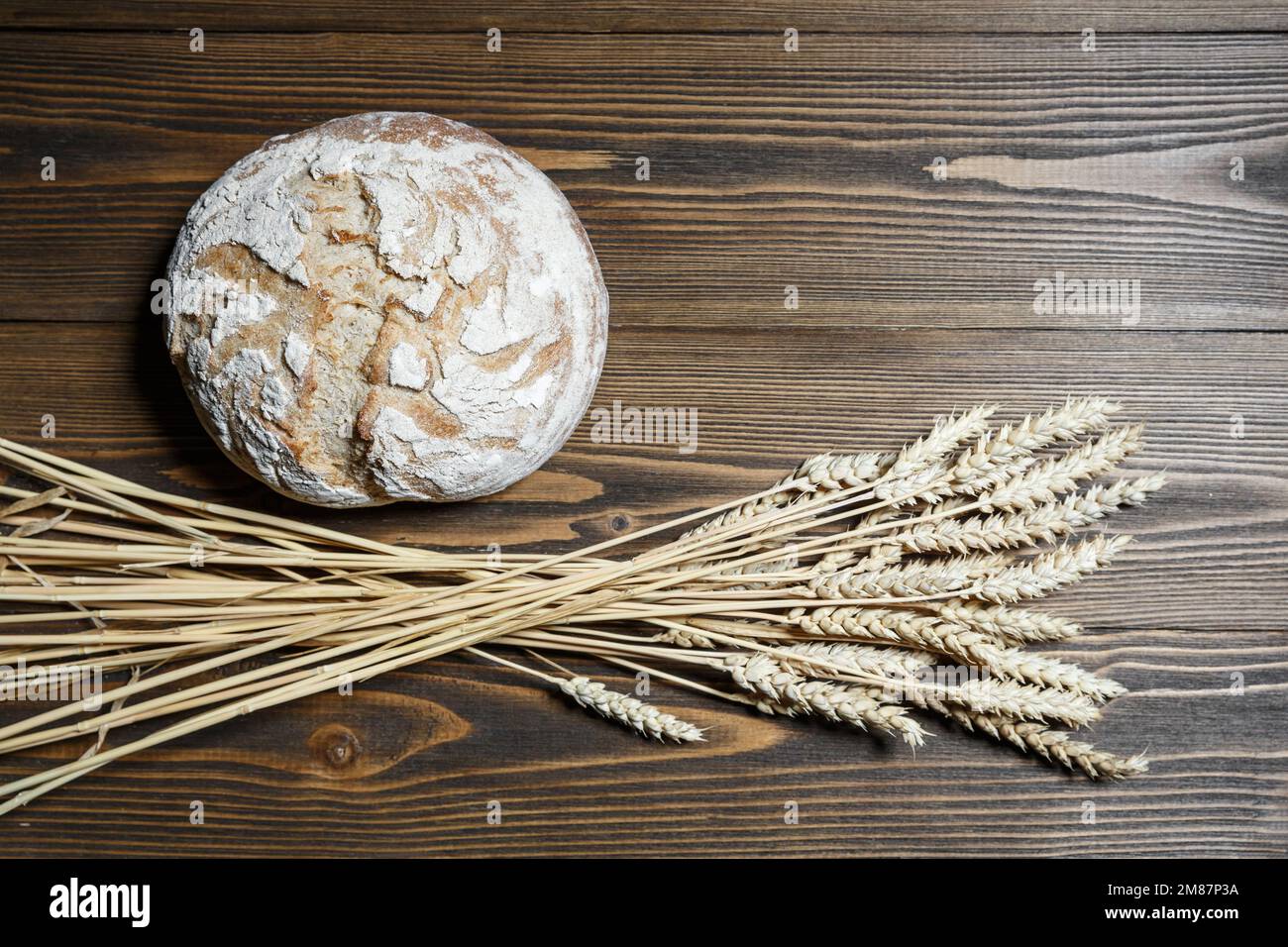 Fresh baked bread loaf and wheat ears lying on a wooden background. Food provision and production concept. Stock Photo