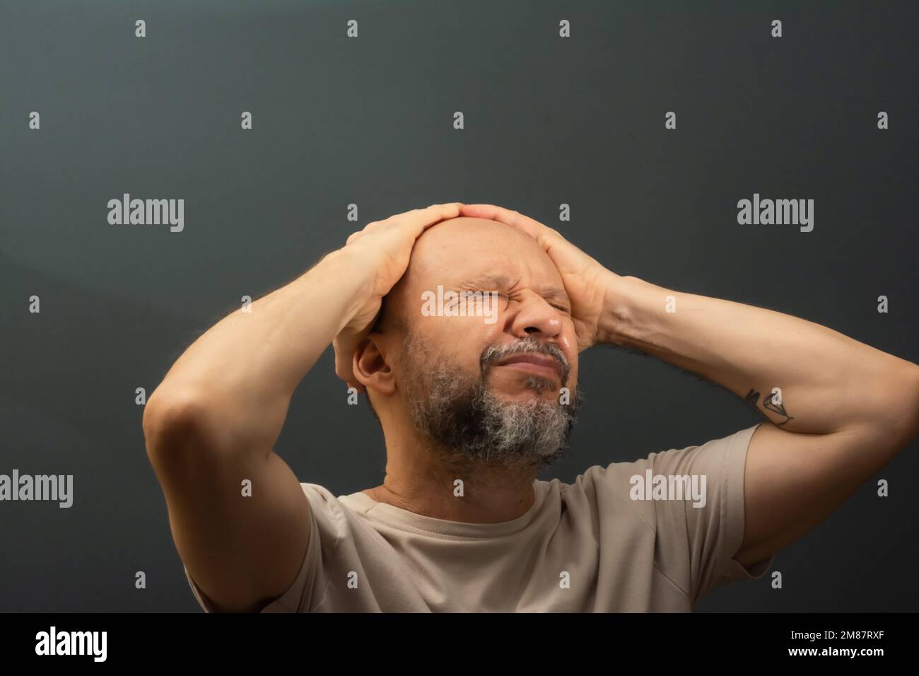 Depressed middle-aged man with both hands on his head isolated on gray ...