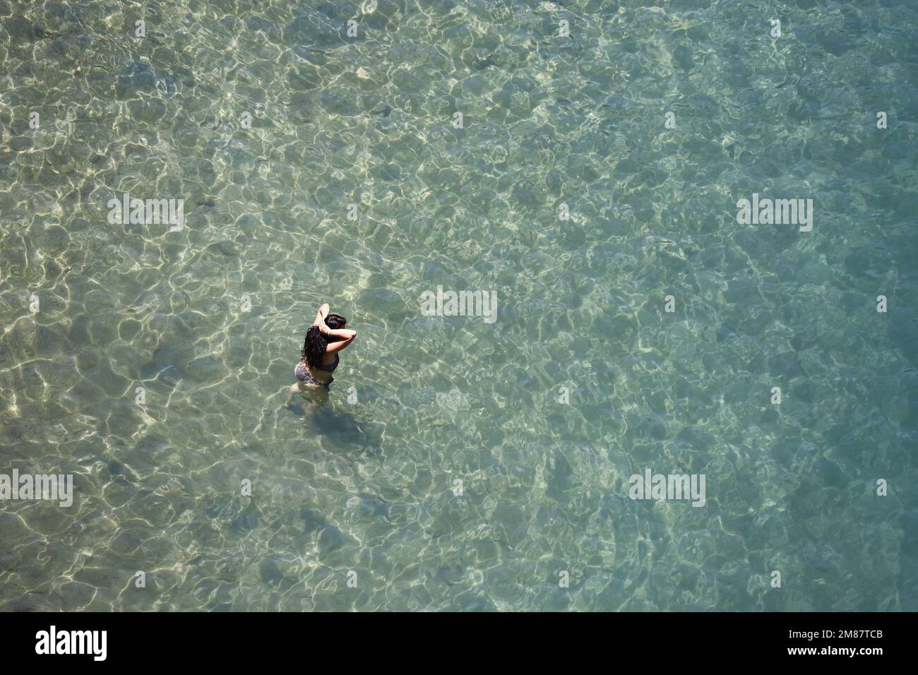 Aerial view to azure sea and woman going to swim in transparent water. Sunny holidays, beach vacation Stock Photo