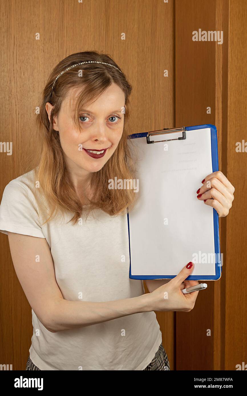 Young beautiful woman holding clip board with empty white paper in her hands Stock Photo