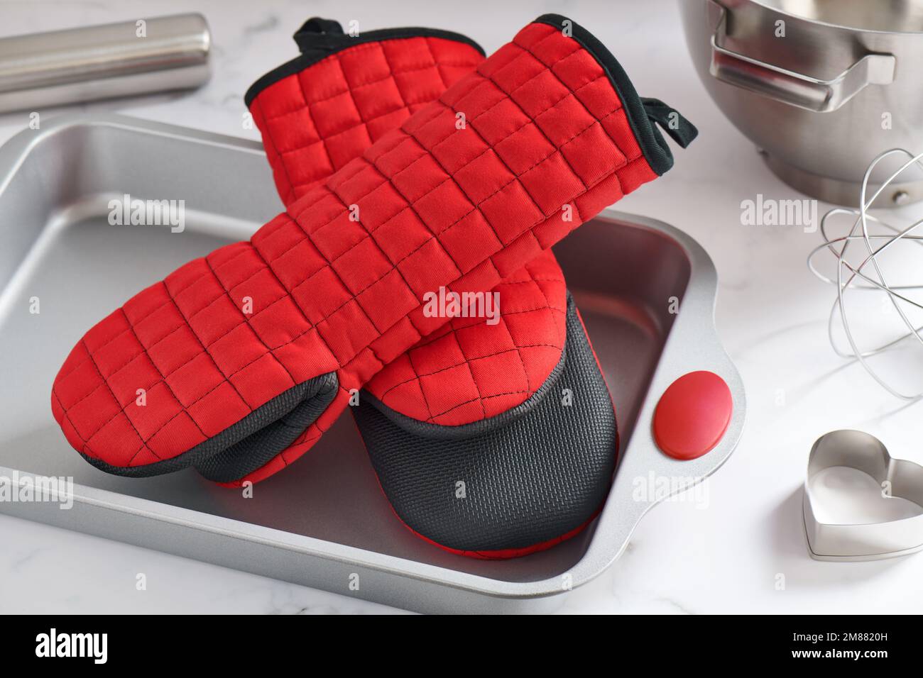 Oven mitts lying in a baking pan surrounded by kitchen utensils Stock Photo