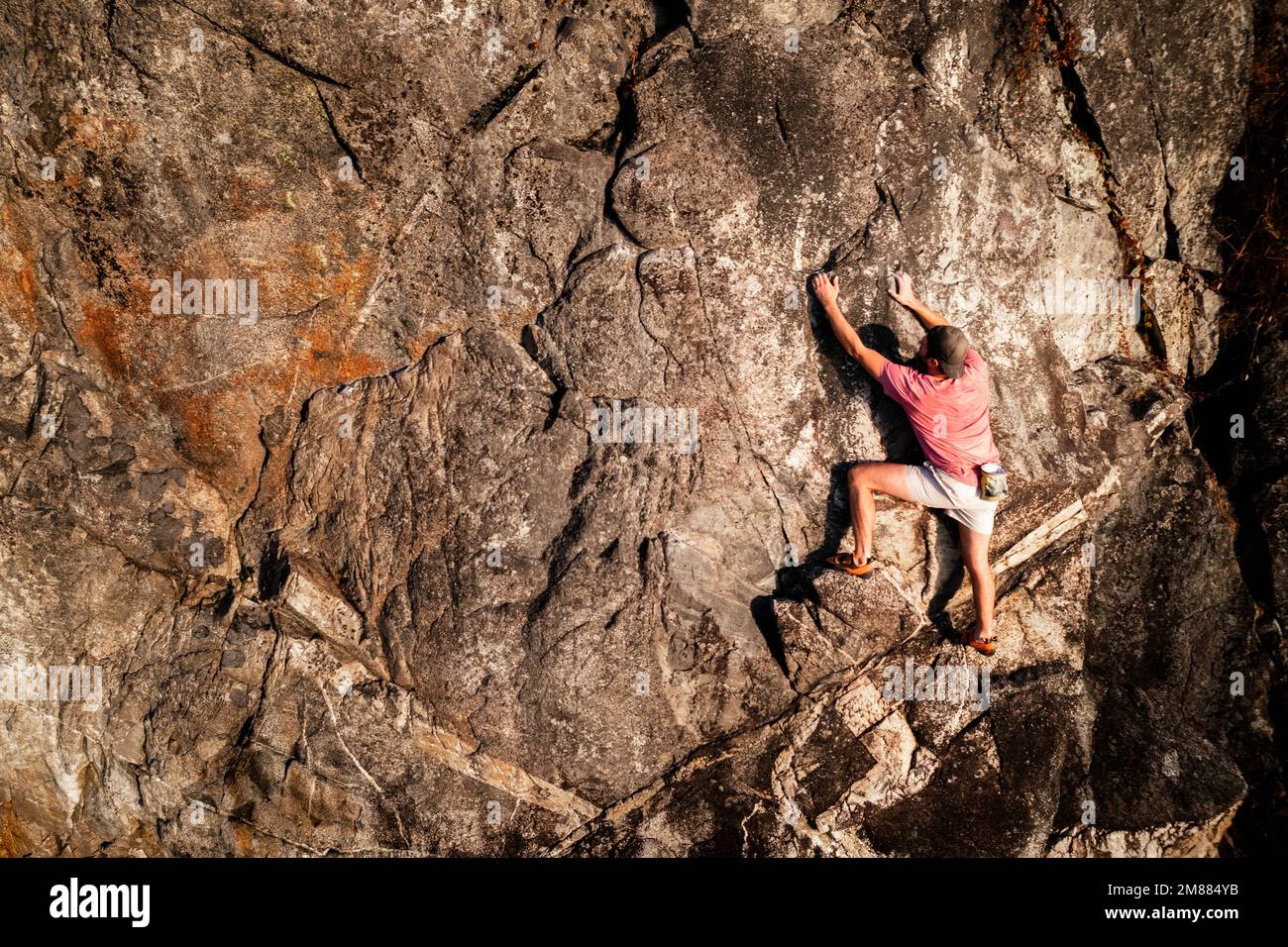 Male rock climber over the ocean, free solo, no rope, adventure sport, rock face, cliff. Stock Photo