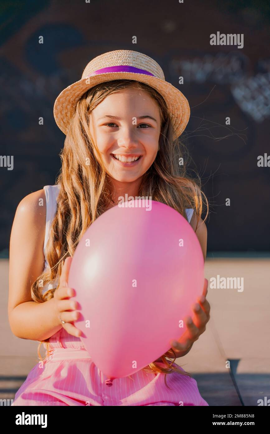 Portrait of a girl in a hat with a pink balloon. She is dressed in pink clothes and her hair is long and loose. Stock Photo