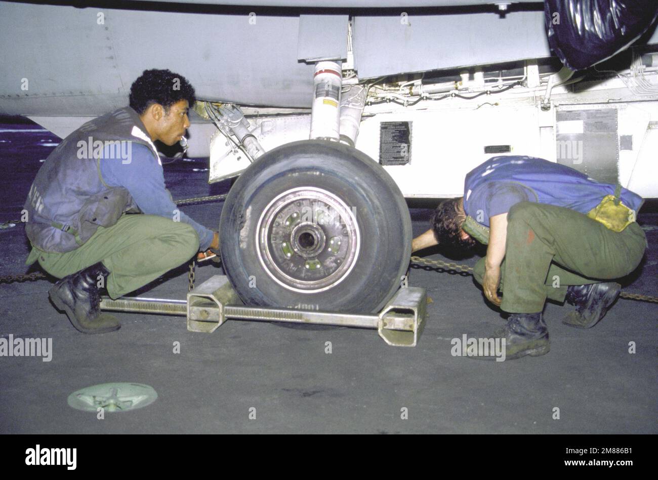 Aircraft handling crewmen secure an aircraft with chocks and chains ...
