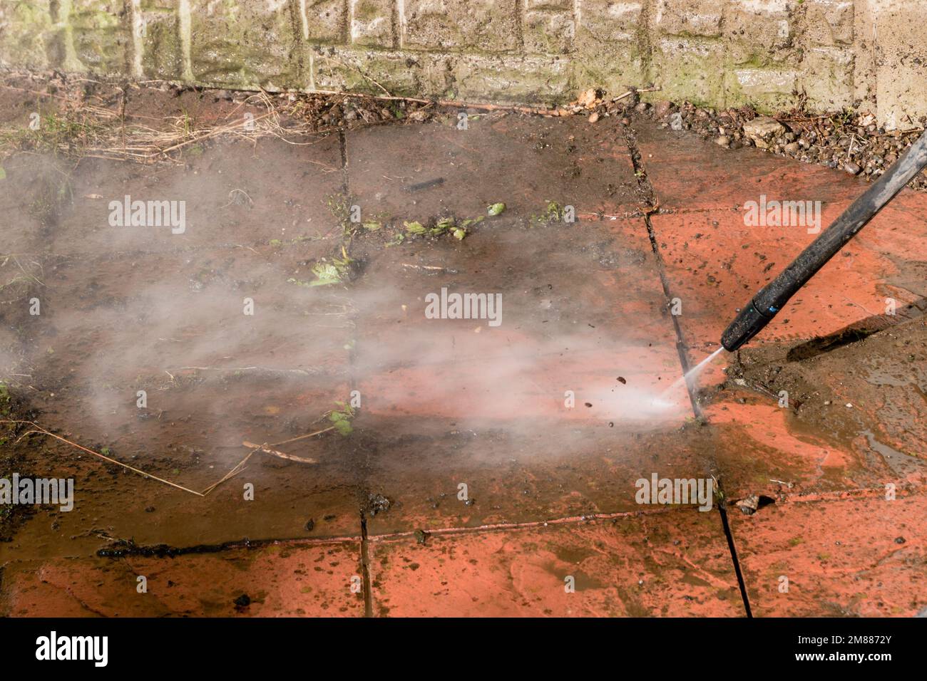 A power pressure washer using a pressurised water stream to clean a dirty stained patio Stock Photo