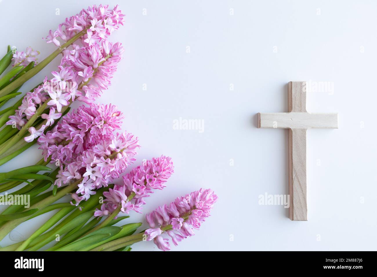 Simple wood Christian cross on a white background with a bouquet of pink hyacinth flowers as a border with copy space Stock Photo