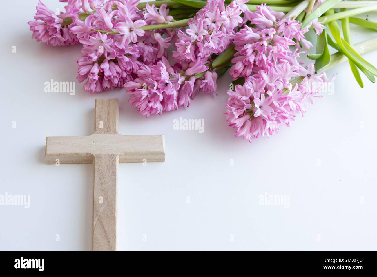 Simple wood Christian cross on a white background with a bouquet of pink hyacinth flowers as a border with copy space Stock Photo