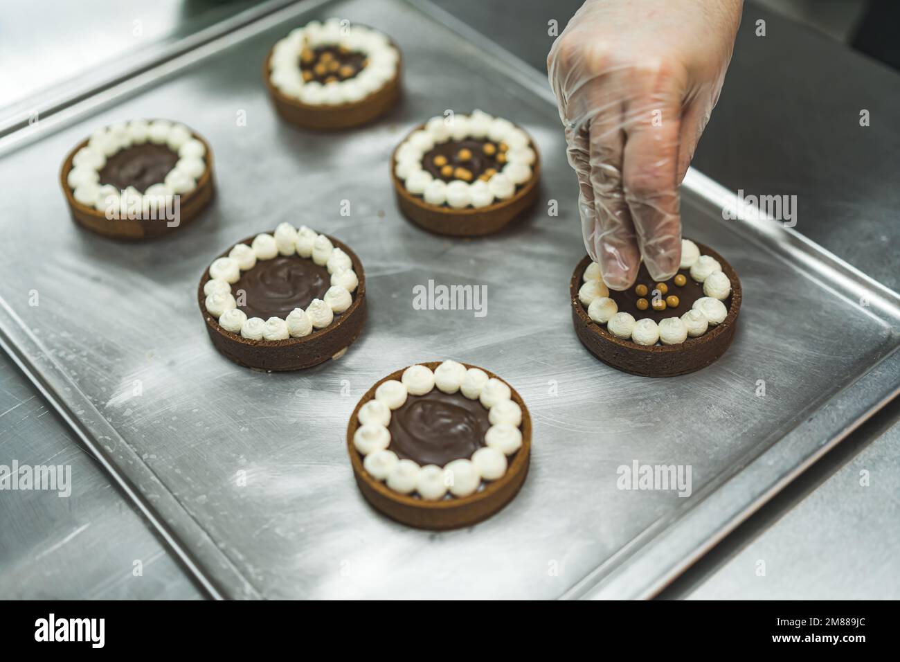 closeup view of a baker's hand adding golden sprinkles to the chocolate cakes at the bakery. High quality photo Stock Photo