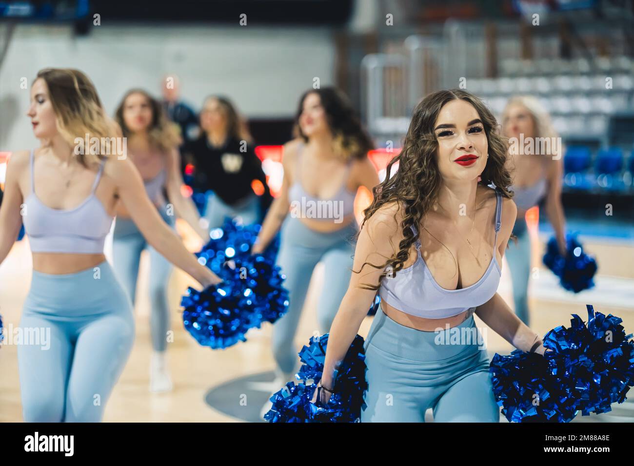 Attractive cheerleaders are dancing with energy and enthusiasm in revealing outfits. They're holding bright blue pom-poms to support their team. Stock Photo