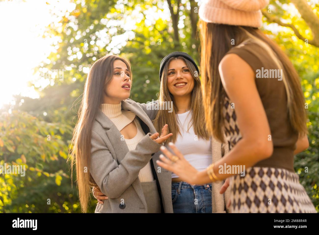 Women friends talking in a park in autumn at sunset, golden hour, lifestyle and autumnal outfit Stock Photo