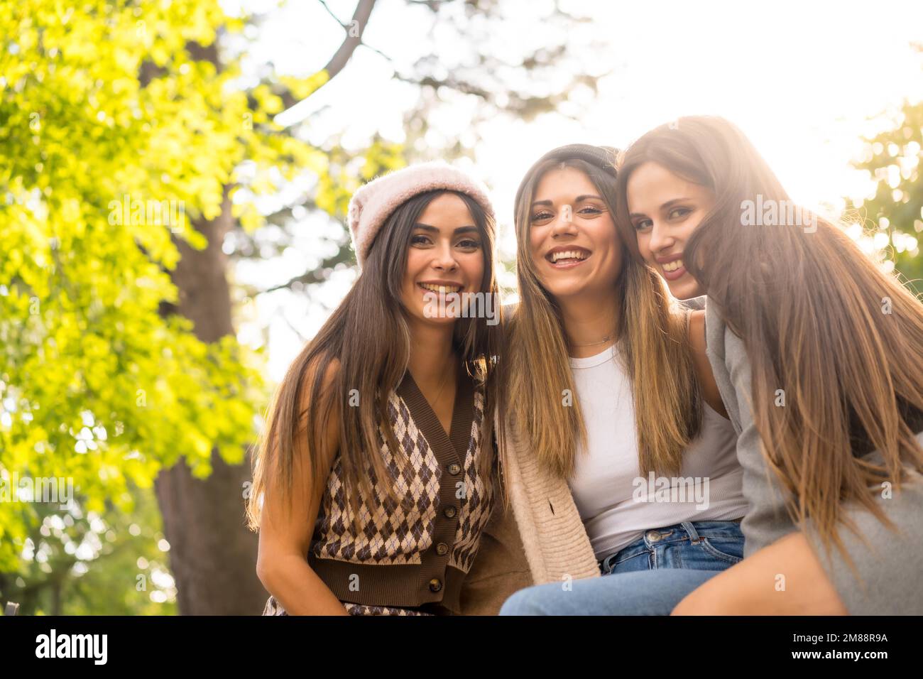 Women friends sitting in a park in autumn, trendy fall lifestyle, carefree, excitement, enjoyment Stock Photo