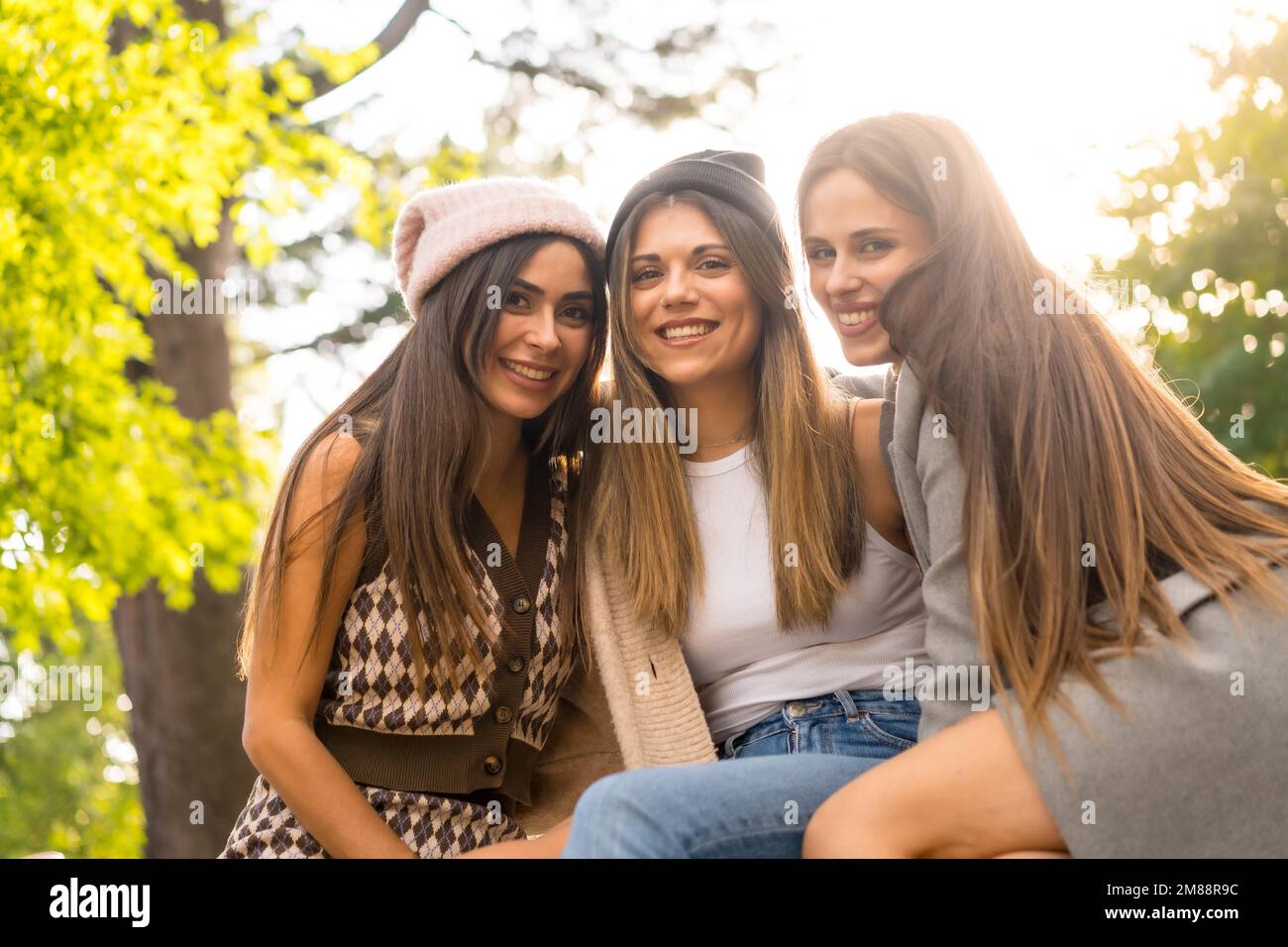 Women friends sitting in a park in autumn, trendy fall lifestyle, carefree, excitement, enjoyment Stock Photo