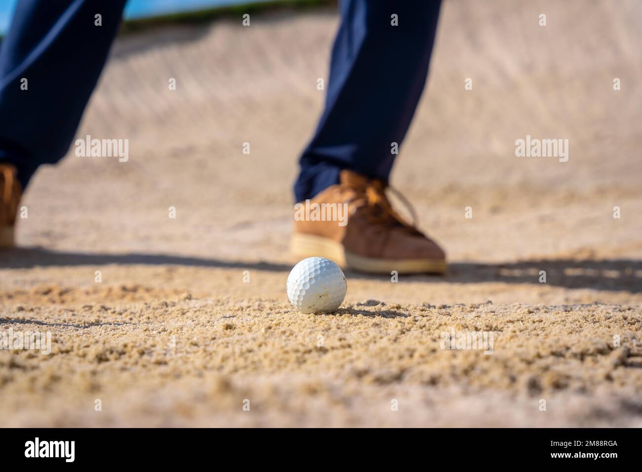 Detail of the feet of a man playing golf, in the bunker hitting the ball with the pitching wedge stick Stock Photo