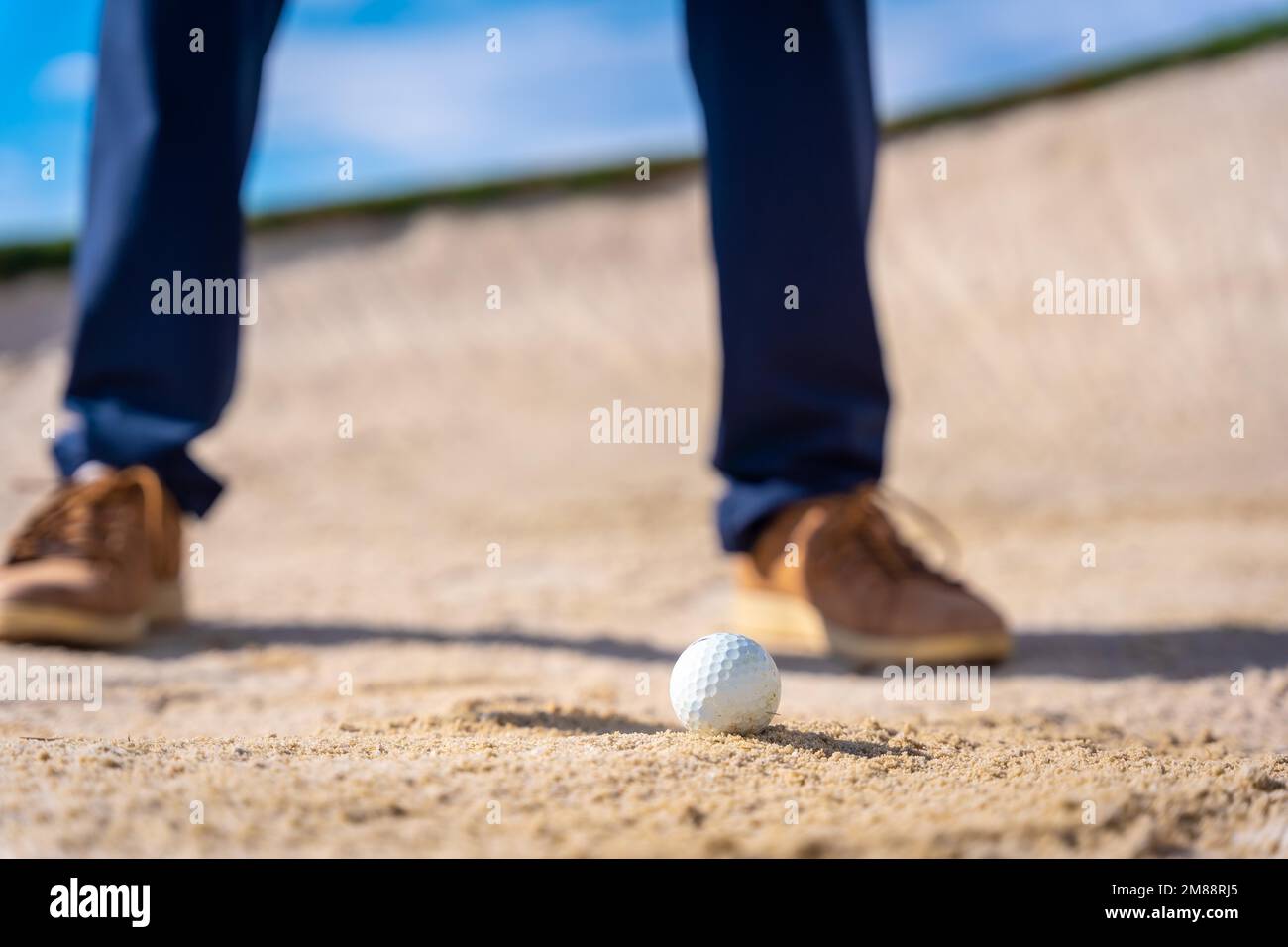 Feet of a man playing golf, in the bunker hitting the ball with the
