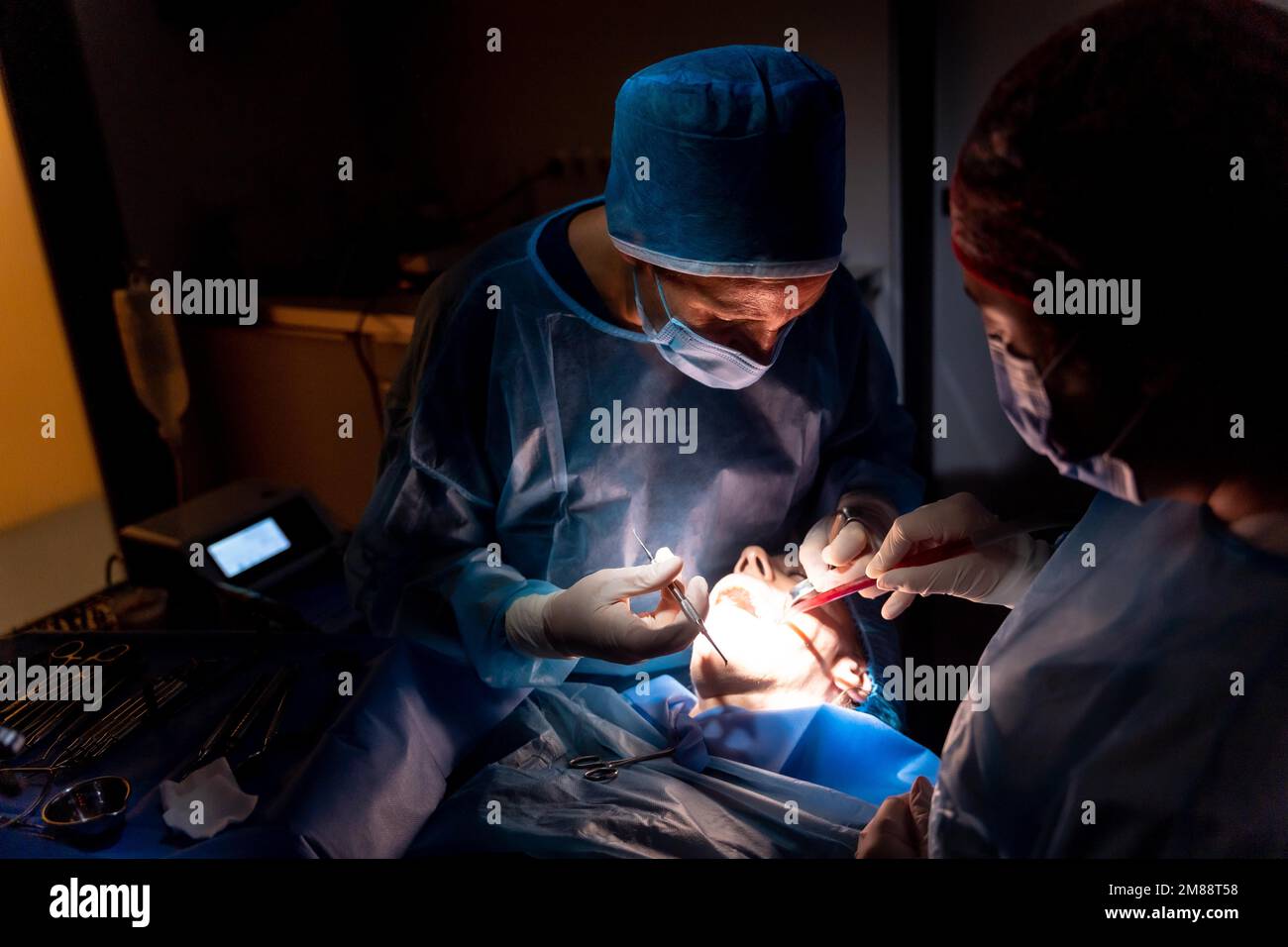 Dental clinic, dentist doctor and the assistant performing an oral operation in the dark Stock Photo