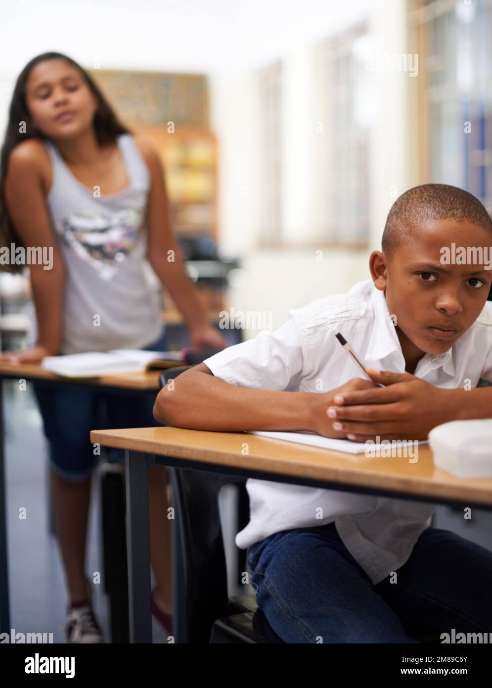 She always copies my work. Portrait of a young boy writing a test while a classmate tries to copy. Stock Photo