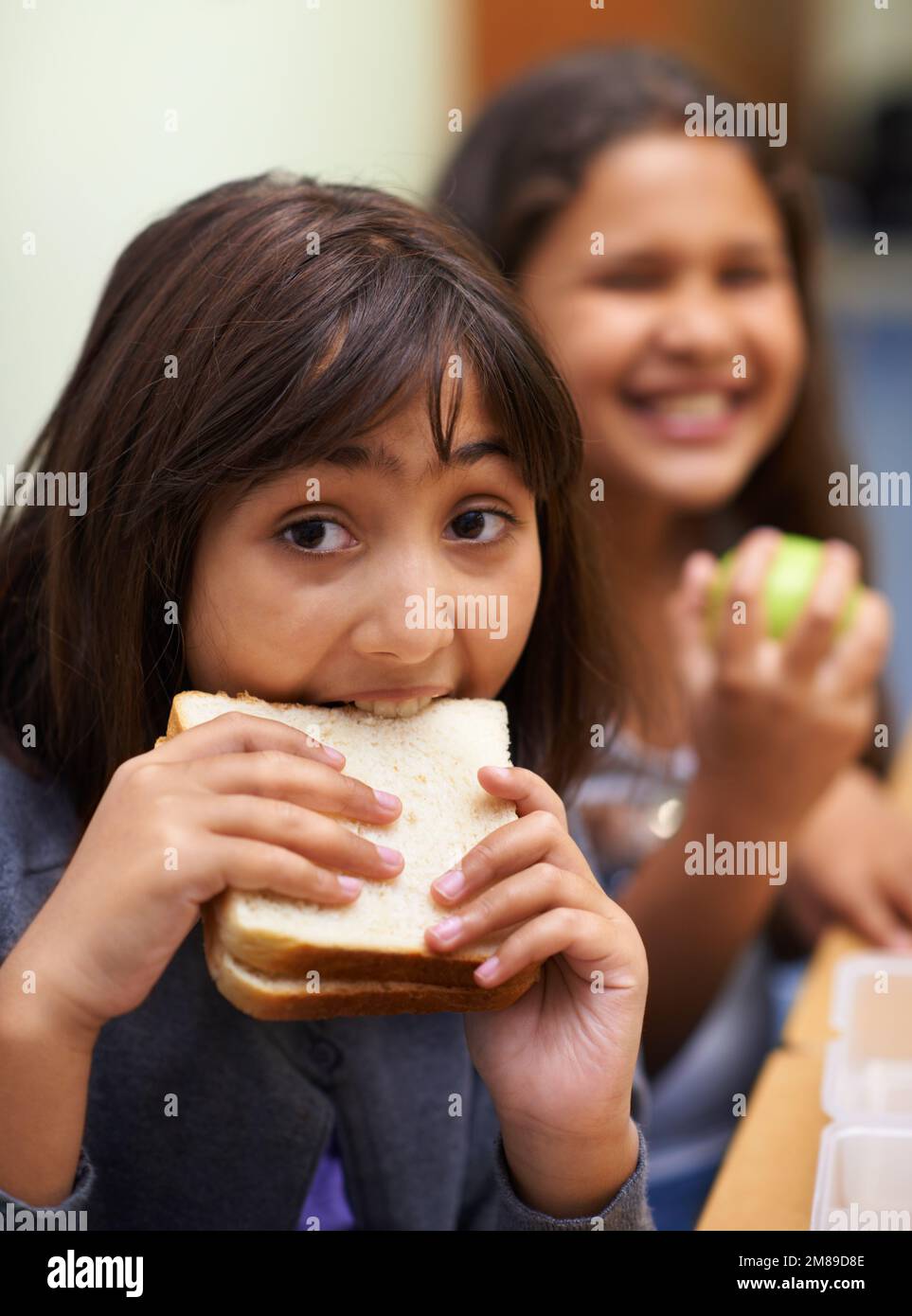Eating the sandwich my mother made for me. Portrait of a young school girl eating her sandwich in the cafeteria during lunchtime. Stock Photo