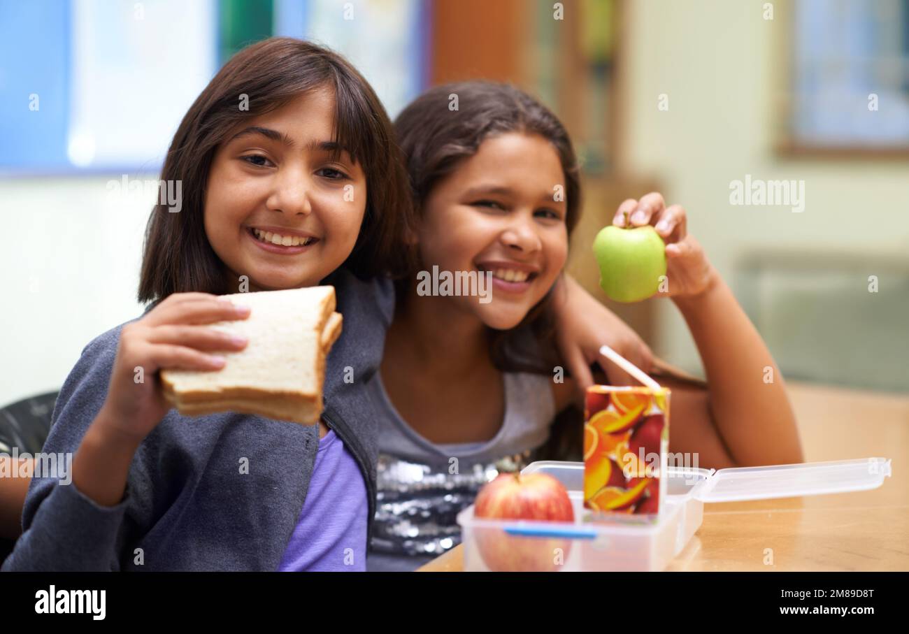 Showing off their lunch. Portrait of two young school girls having lunch in the cafeteria during recess. Stock Photo