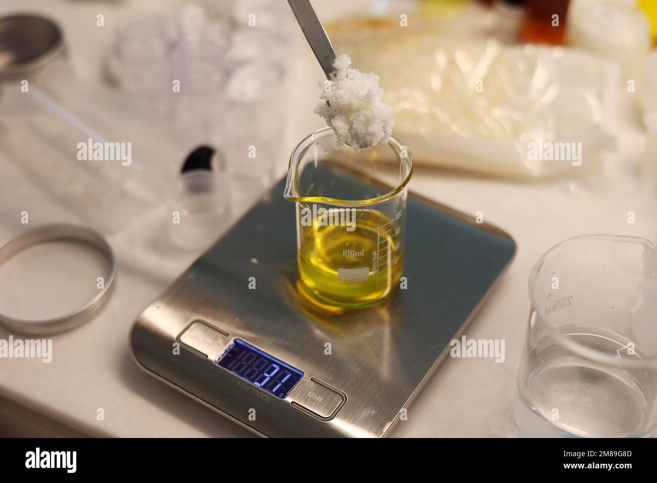 Put an ingredient in the beaker, weigh jojoba oil in the beaker on the electronic scale, spoon the ingredient laboratory Stock Photo