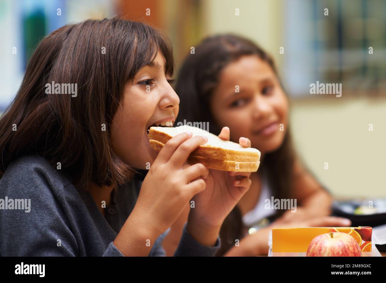 Enjoying a sandwich during recess. A young school girl eating her sandwich in the cafeteria during lunchtime. Stock Photo