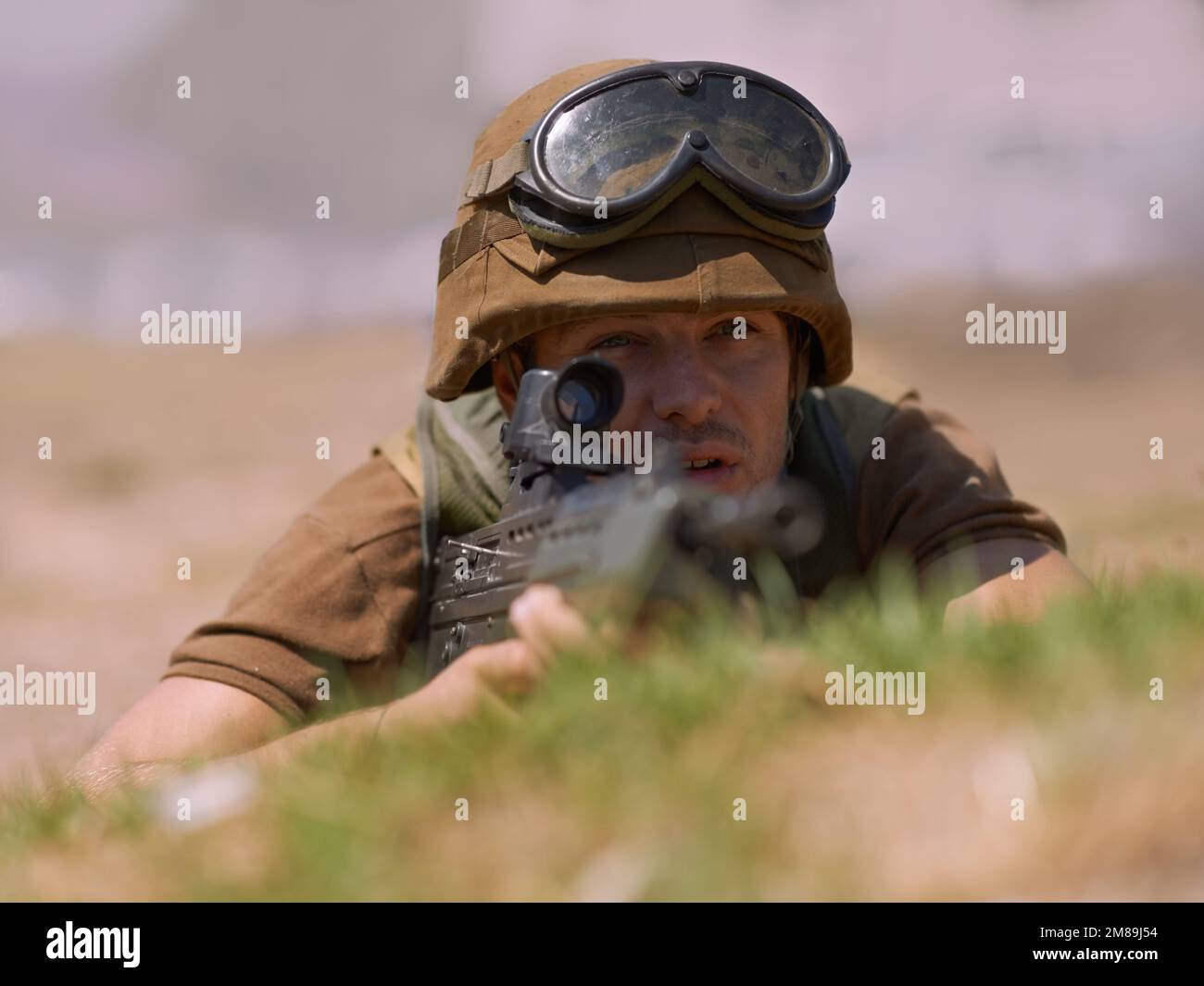Trained to aim. A young soldier aiming with his rifle while lying on the ground. Stock Photo
