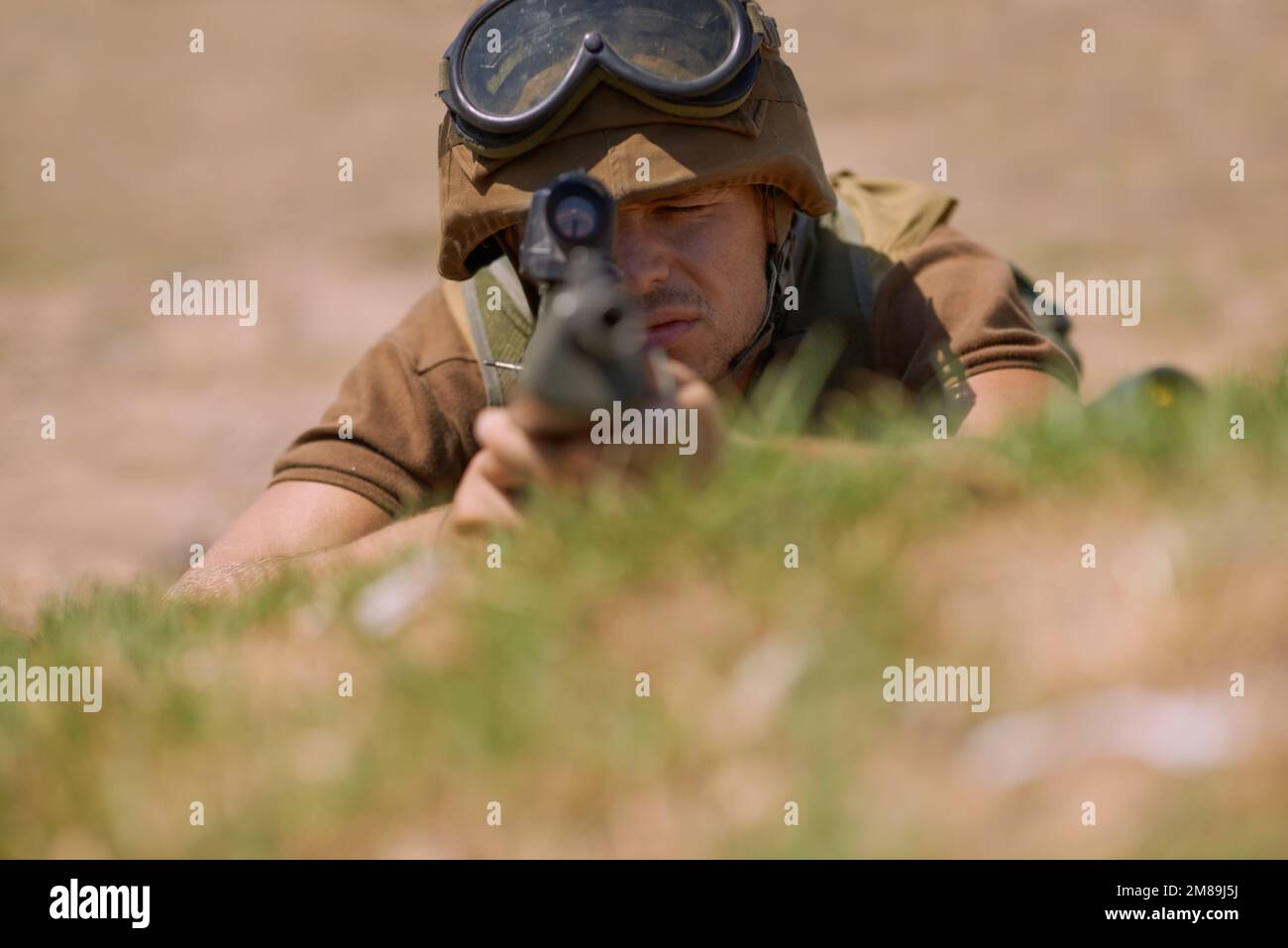 Aiming at you. A young soldier aiming with his rifle while lying on the ground. Stock Photo