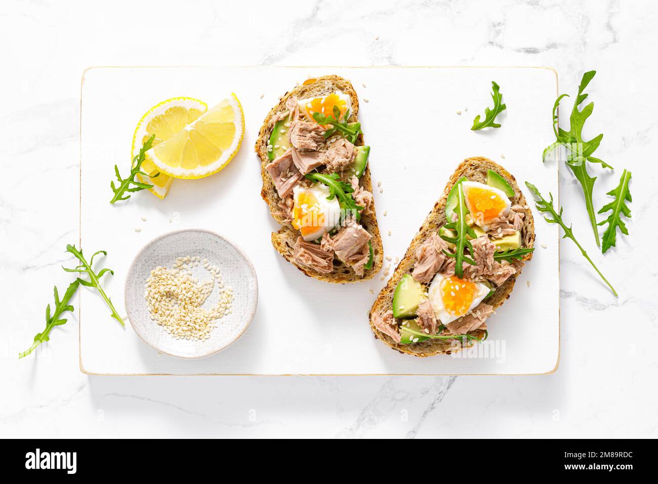 Tuna toast. Open sandwiches with whole grain bread, canned tuna, boiled egg, avocado and arugula. Top view Stock Photo