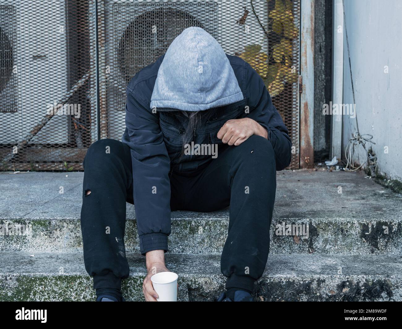 Stressed hungry homeless man sitting on city street waiting for help and money. Stock Photo