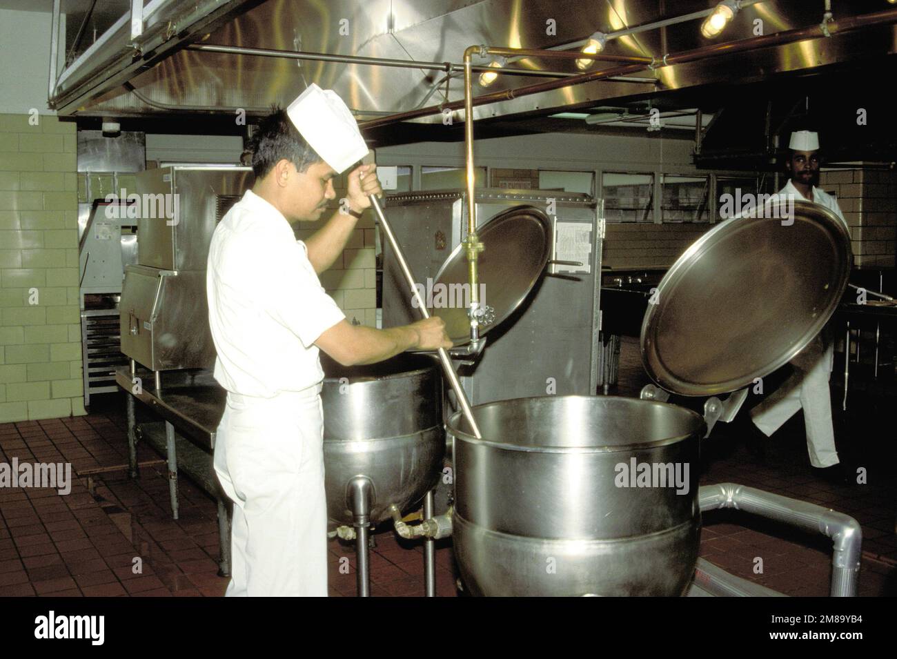 An airman apprentice stirs a soup kettle in the kitchen of the enlisted mess. Base: Naval Air Station, Oceana State: Virginia (VA) Country: United States Of America (USA) Stock Photo