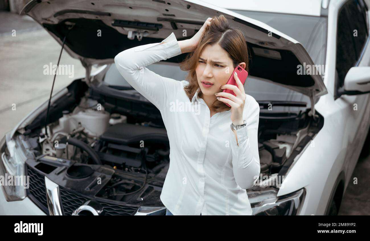 Young woman calling emergency help near broken car on road. Stock Photo