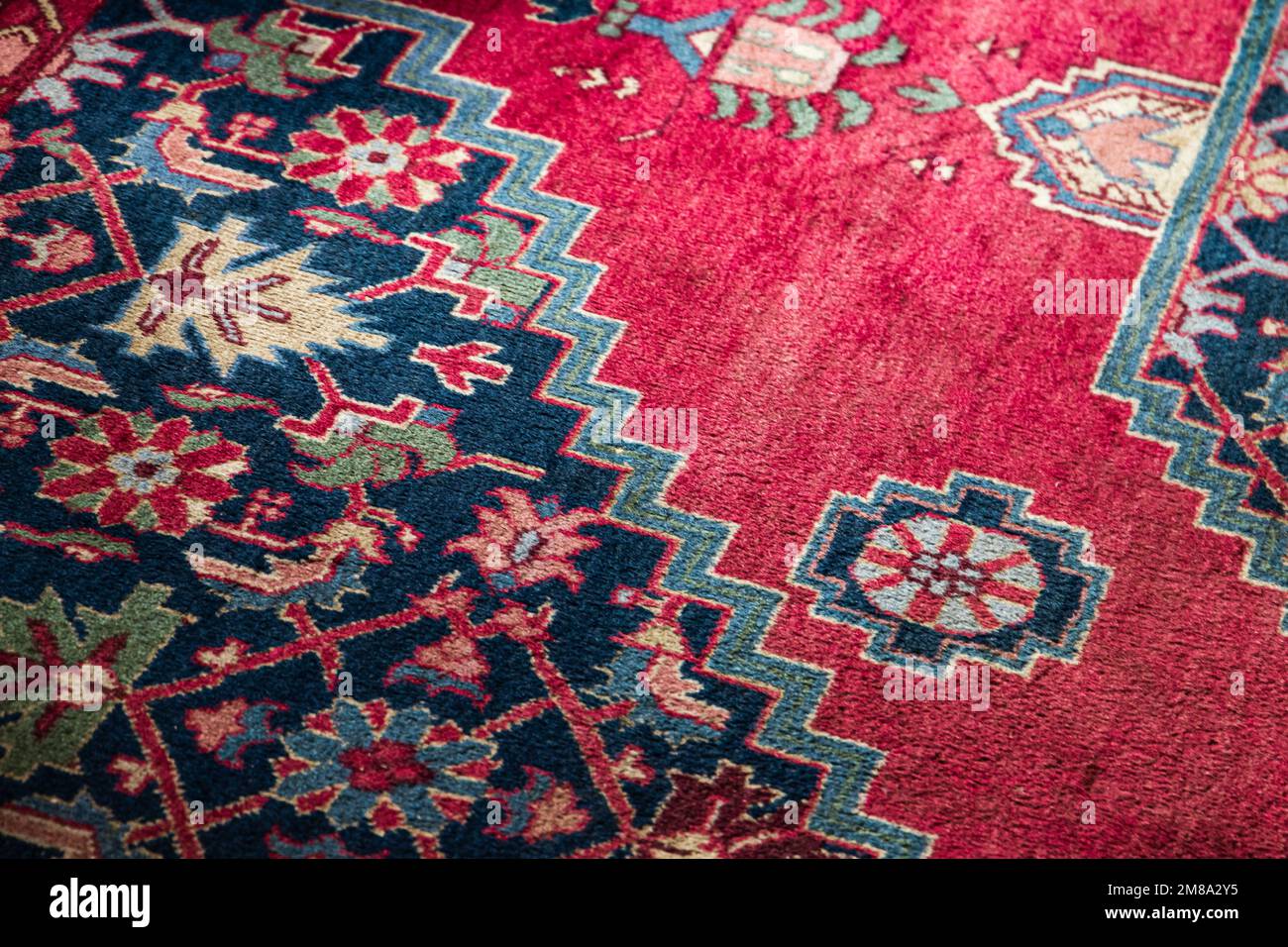 Oriental woolen carpet with traditional colorful ornaments over red background. Close up photo Stock Photo