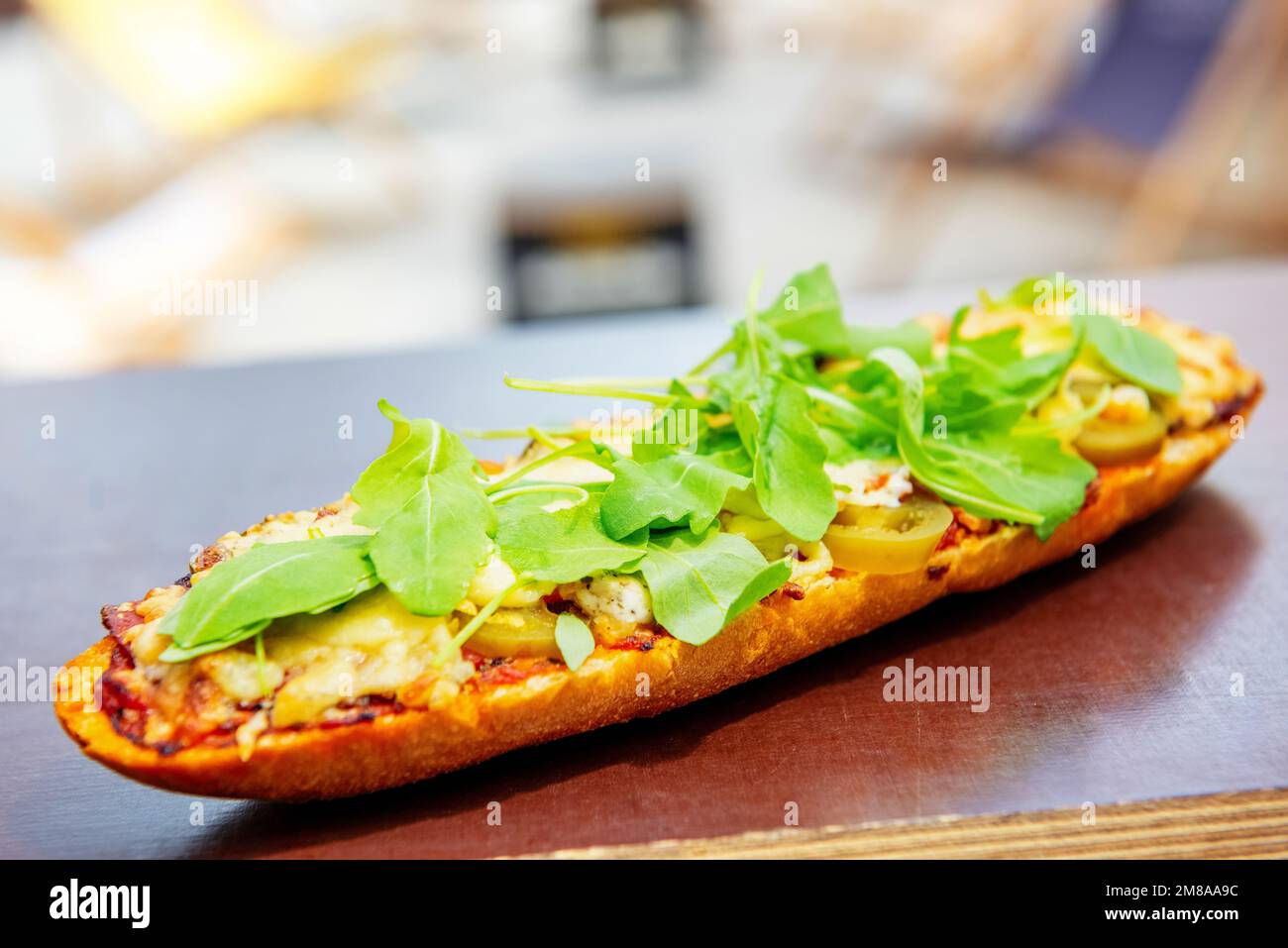 baguette with tomato sauce, meat, jalapeno and arugula baked with cheese on a table outdoor. popular street fast food Stock Photo
