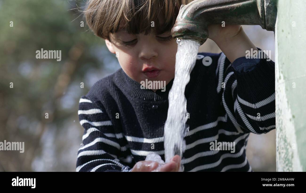 Closeup of flowing water faucet child hand and mouth drinking outdoors