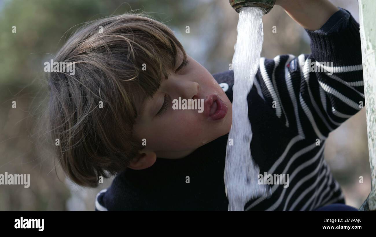 Closeup of flowing water faucet child hand and mouth drinking outdoors