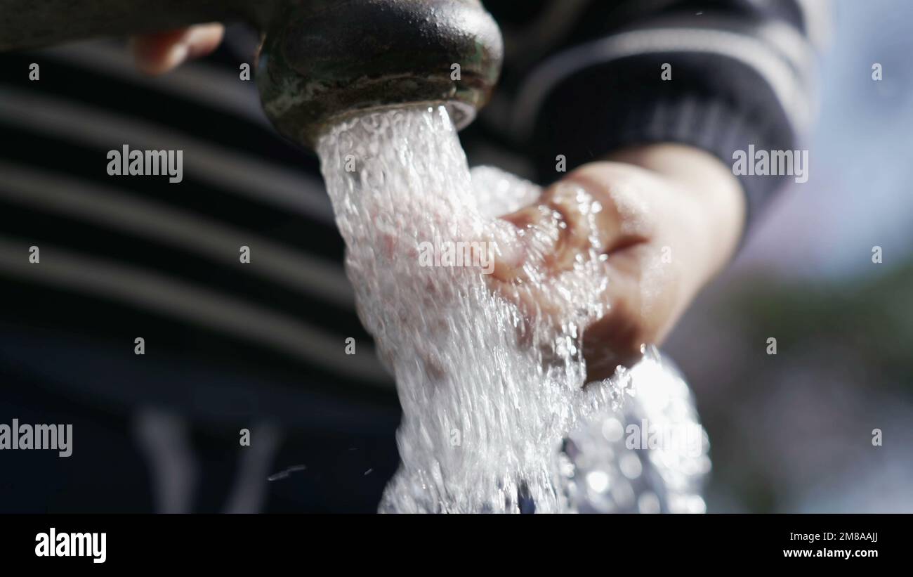 Closeup of flowing water faucet child hand and mouth drinking outdoors