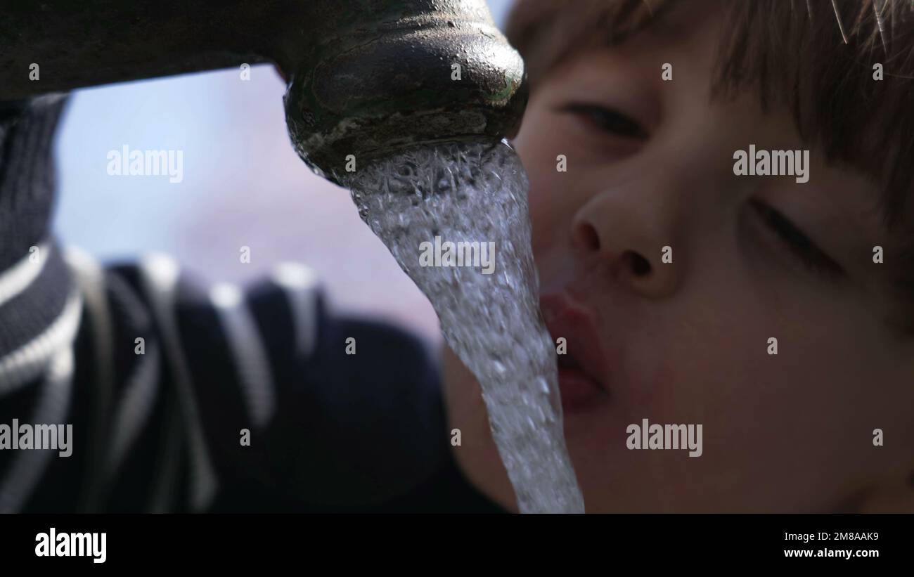 Closeup of flowing water faucet child hand and mouth drinking outdoors