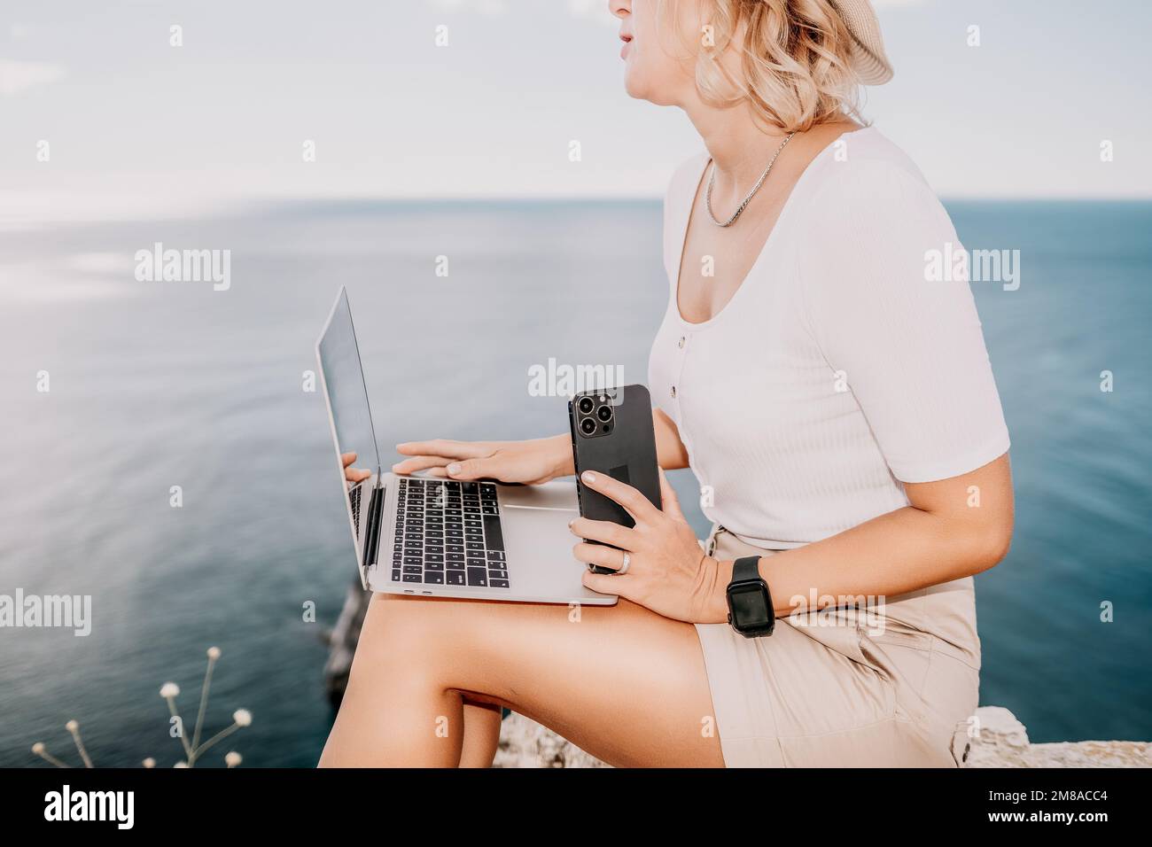 Digital nomad, Business woman working on laptop by the sea. Pretty lady typing on computer by the sea at sunset, makes a business transaction online Stock Photo