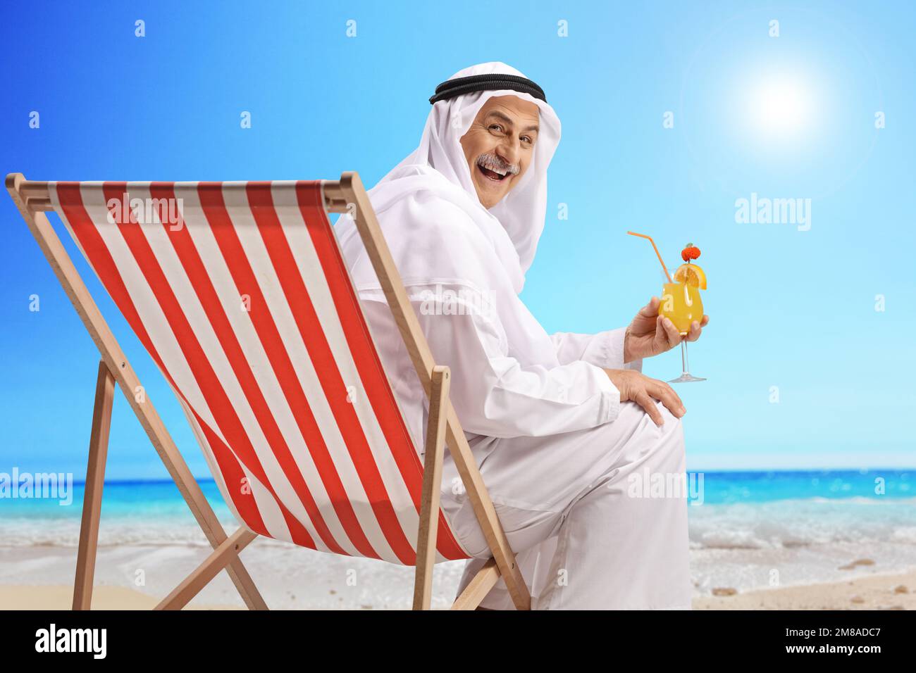 Arab man in a robe sitting on a beach with a cocktail and smiling Stock Photo