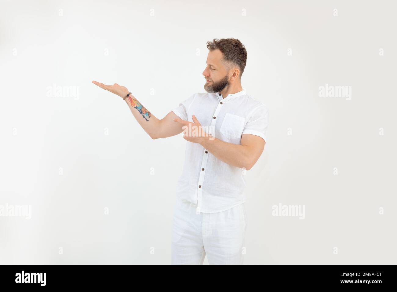 Sporty middle-aged bearded man standing, raising hand with open palm, pointing with forefinger on white background. Stock Photo