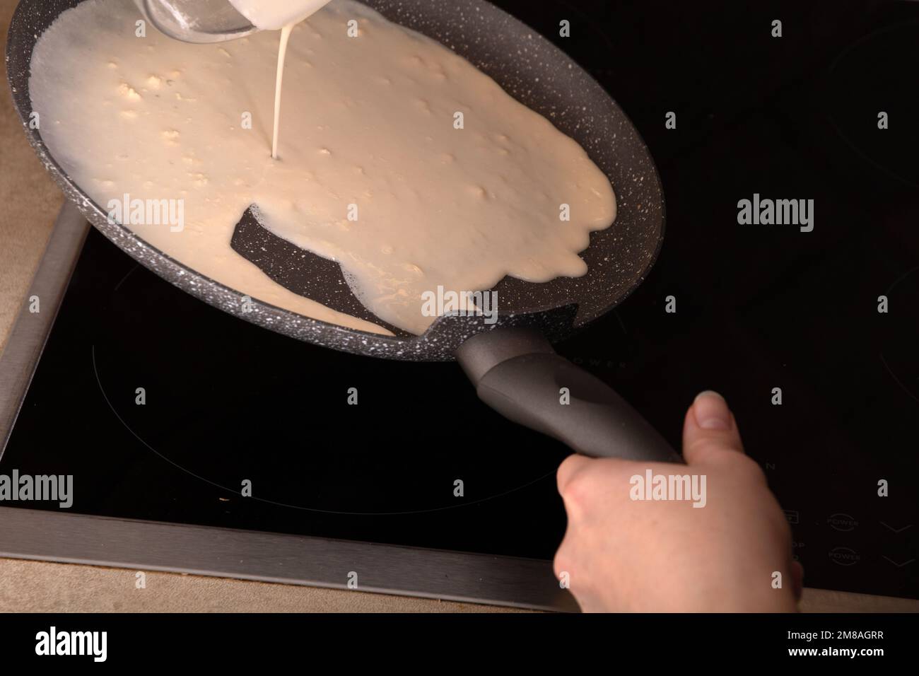 photo of pouring pancake batter on a hot frying pan in the kitchen Stock Photo