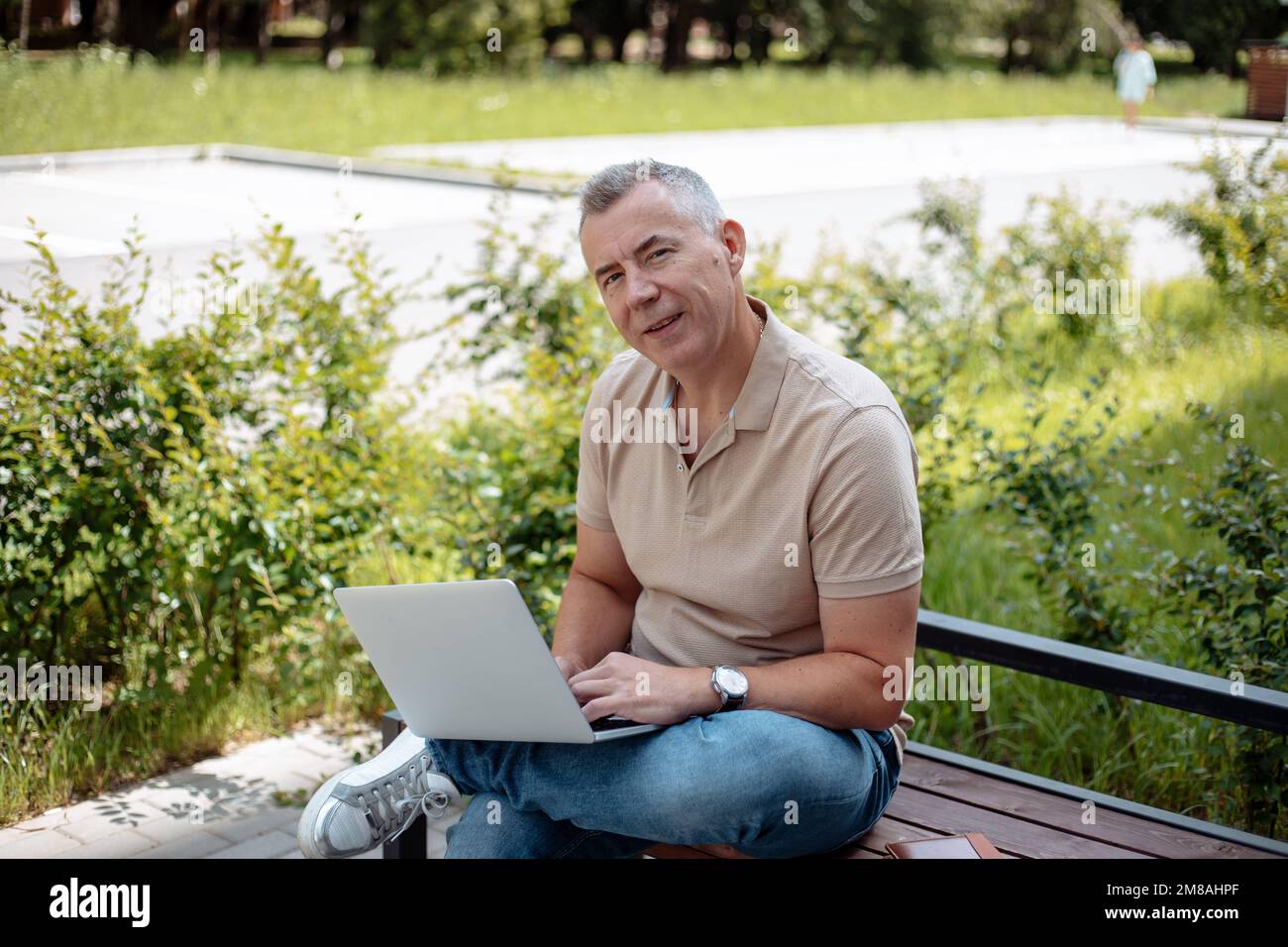 Expressive, charismatic senior gray haired businessman using laptop, wireless modern technology sitting on bench in park Stock Photo